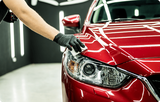 Gloved hand polishing red car headlight